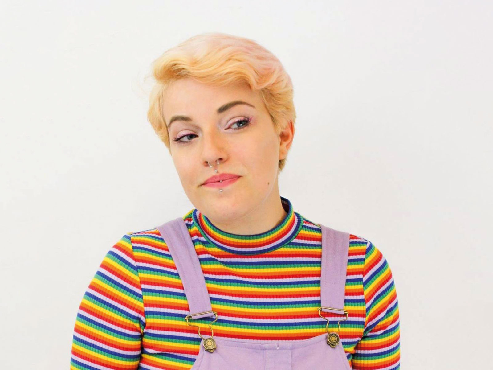 Emrys Travis is the Royal Society of Chemistry's disability and accessibility specialist. Emrys is pictured in a profile style wearing a rainbow-coloured top and lilac dungarees