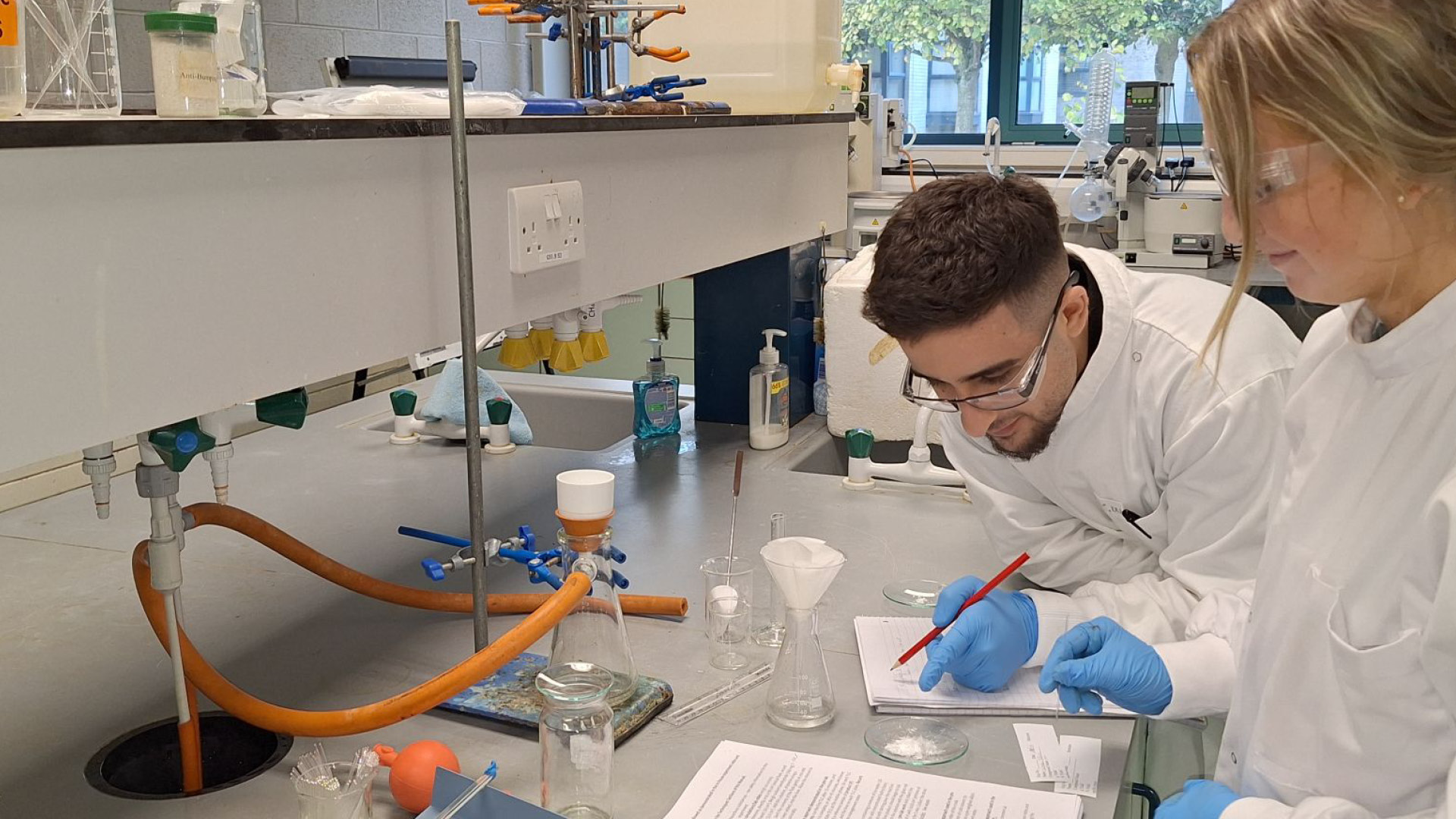 Virtual Labs Team students in white lab coats writing down experiment results