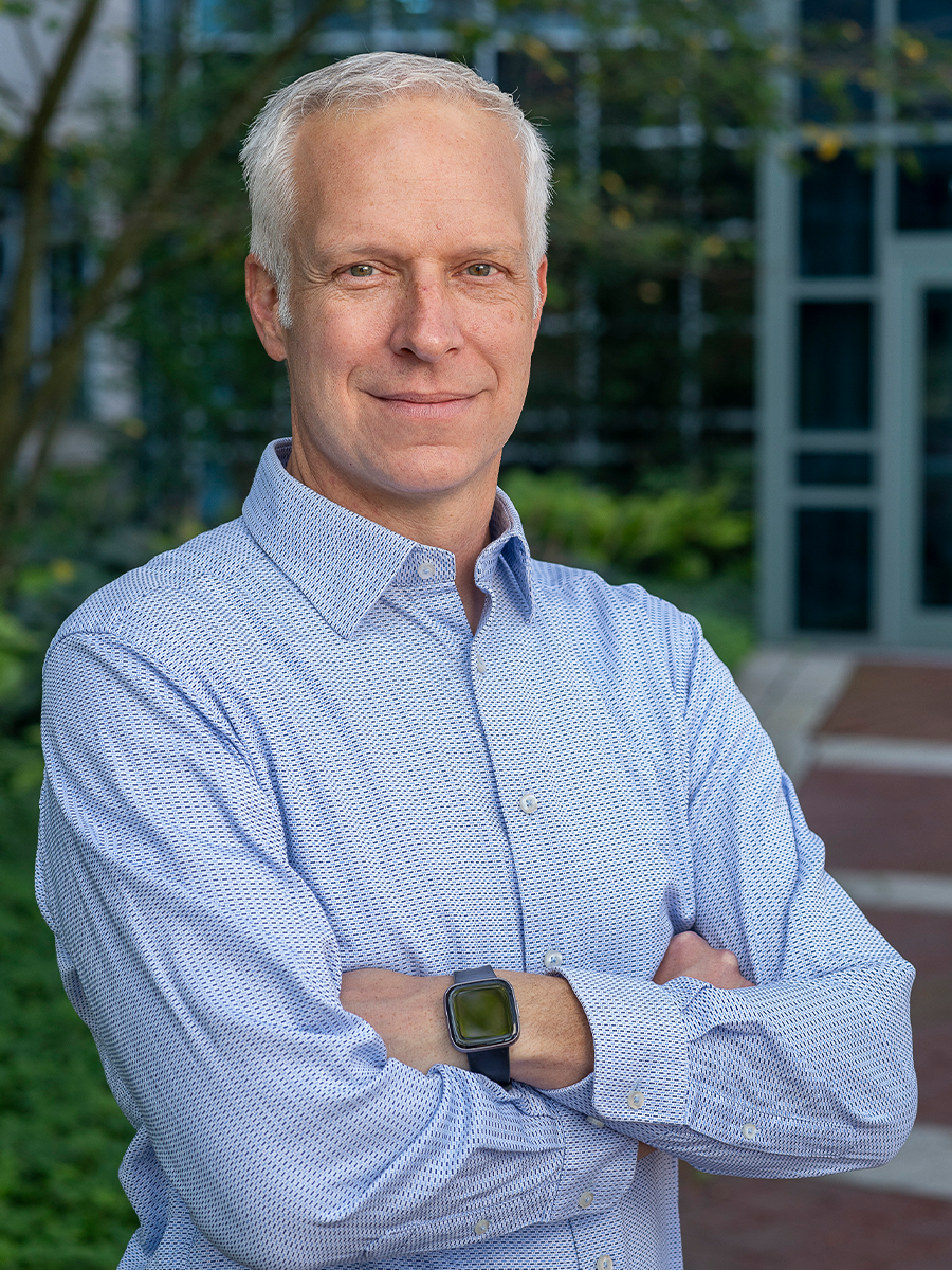 Alfred Crosby, smiling, wearing a blue formal shirt, hands folded across chest