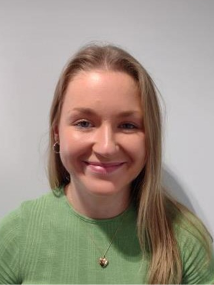 Hannah Hamilton smiling, wearing a light green, textured crew-neck top set against a grey background.