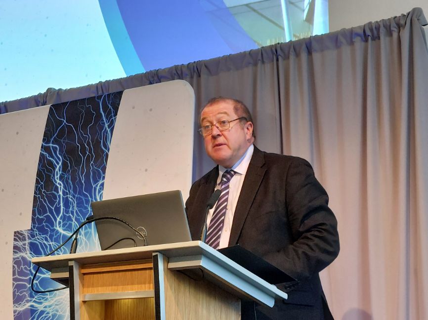 Graeme Dey MSP faces out towards the crowd (out of shot) while standing in front of a lecturn and a laptop