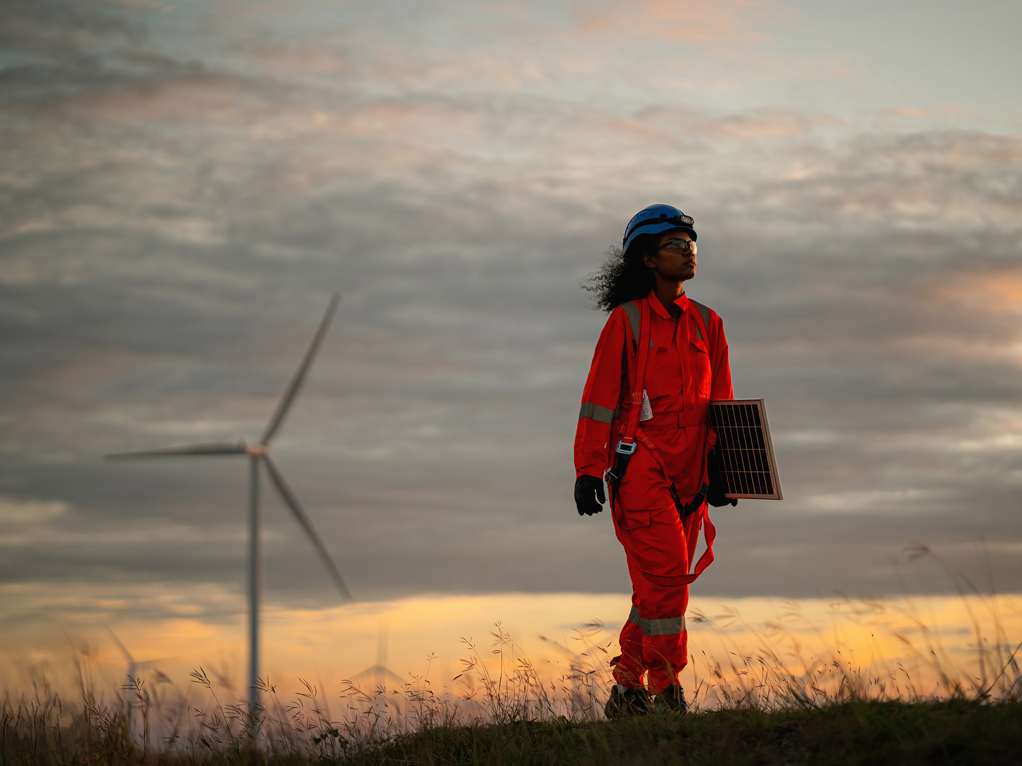 Woman wearing high visibility clothing walking in a field with a wind turbine in the background