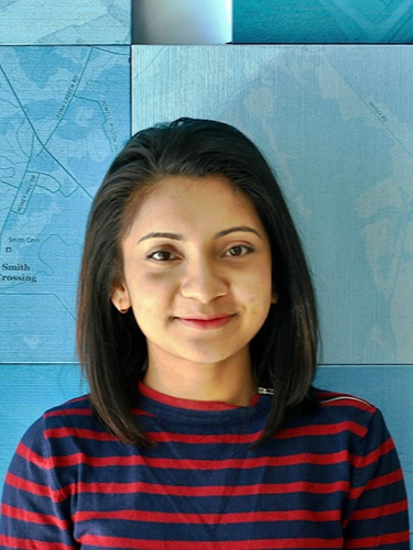 Aditi Dey Poonam smiling with shoulder-length dark hair, positioned in the centre against a light blue background.