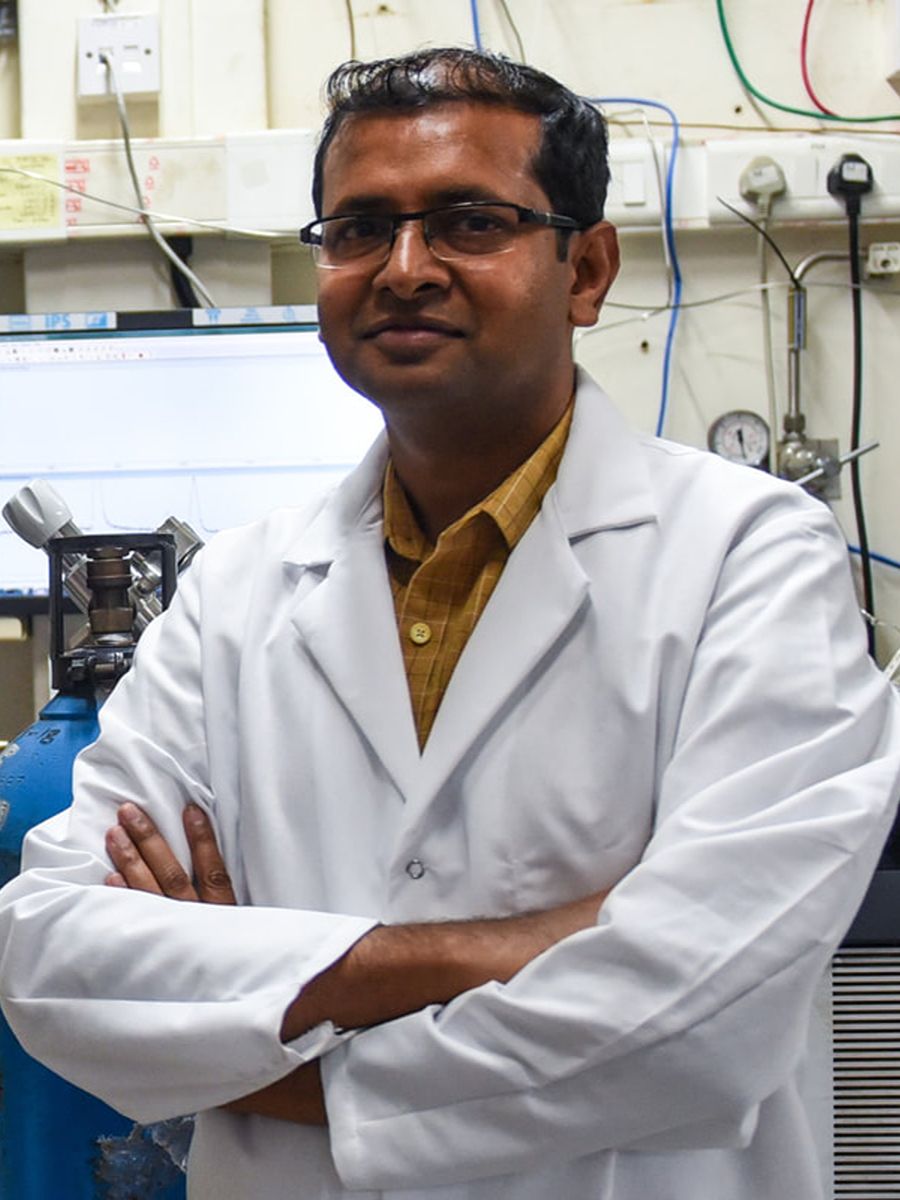 Vivek Polshettiwar wearing a white lab coat and glasses in a lab