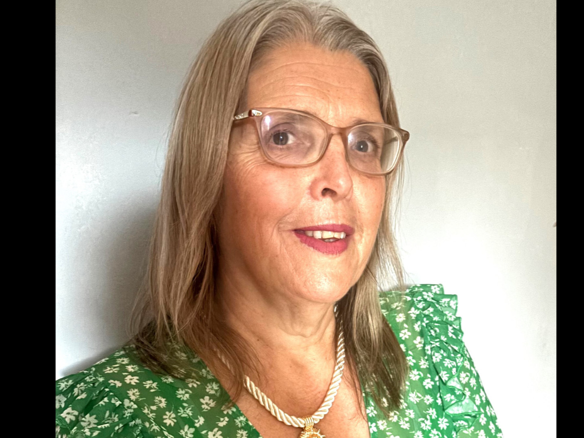 Joanne Davies smiling to camera wearing glasses and a green floral dress