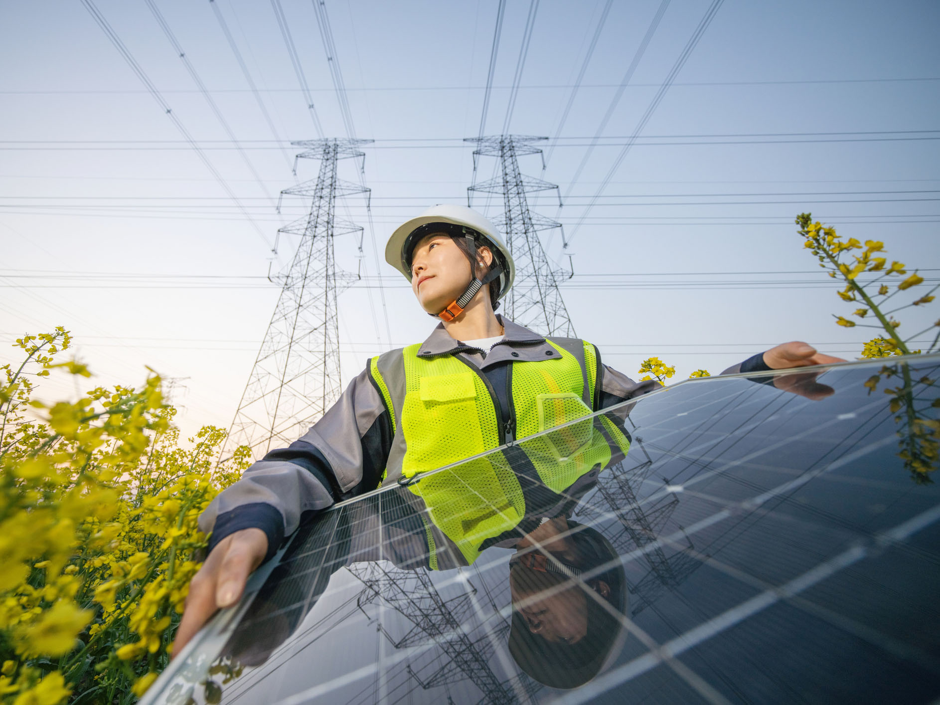 Female engineer holds a solar power panel outside with pylons in the background