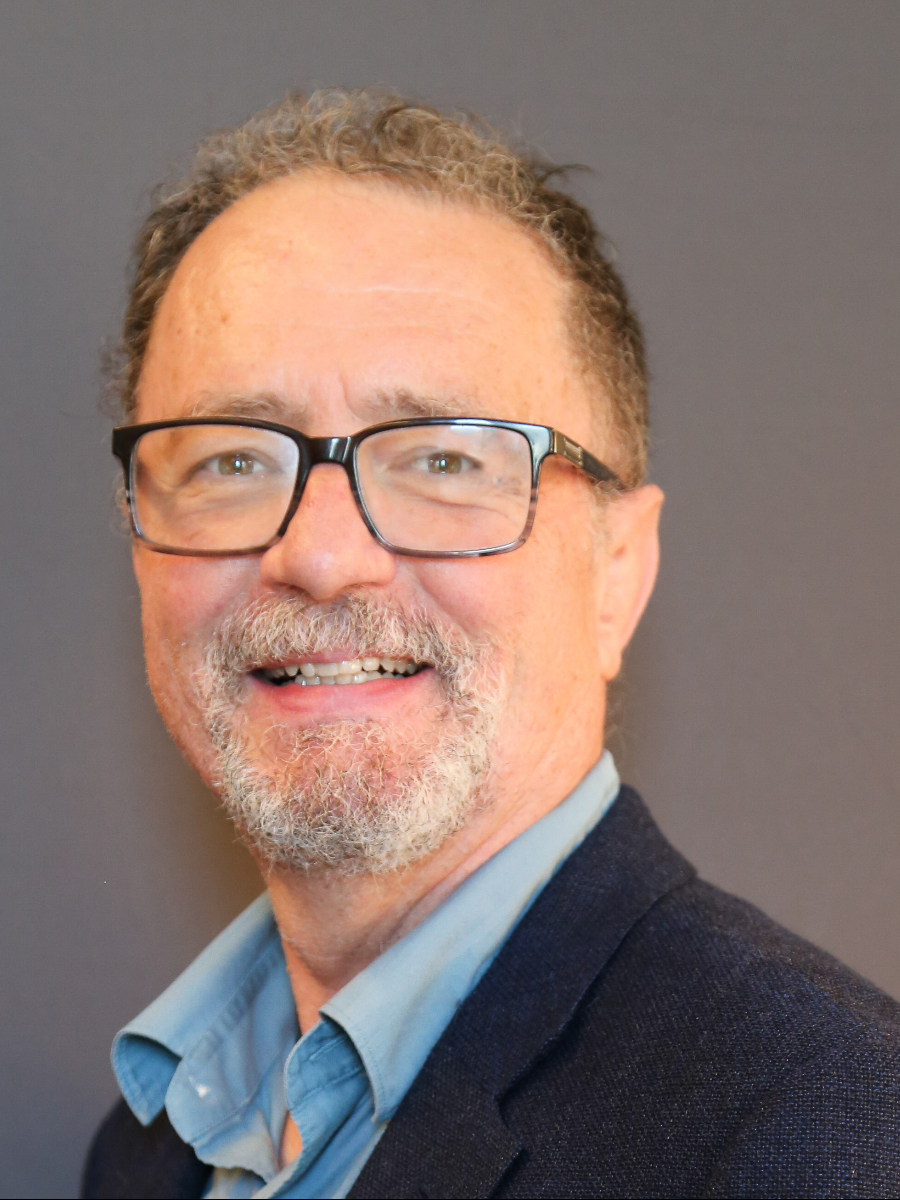  Brian Sheldon smiling to camera wearing glasses and suit, with a beard