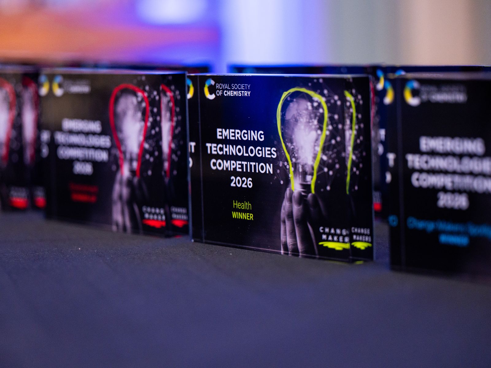 A series of four plaques sat on a table with imagery on each that reads "Emerging Technologies Competition 2026"