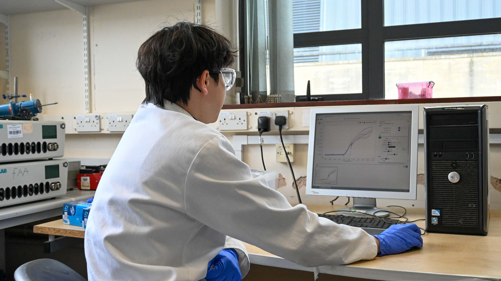Biocatalytic Nitro Hydrogenations team member in lab coat and gloves looking at data on a computer