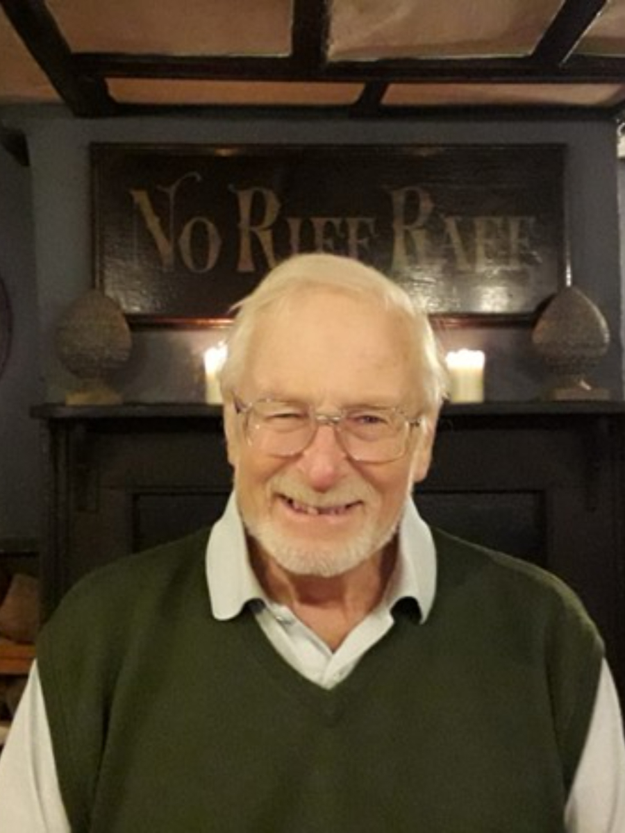 Dr Clifford John Harris wearing glasses and shirt in home setting, smiling broadly to camera