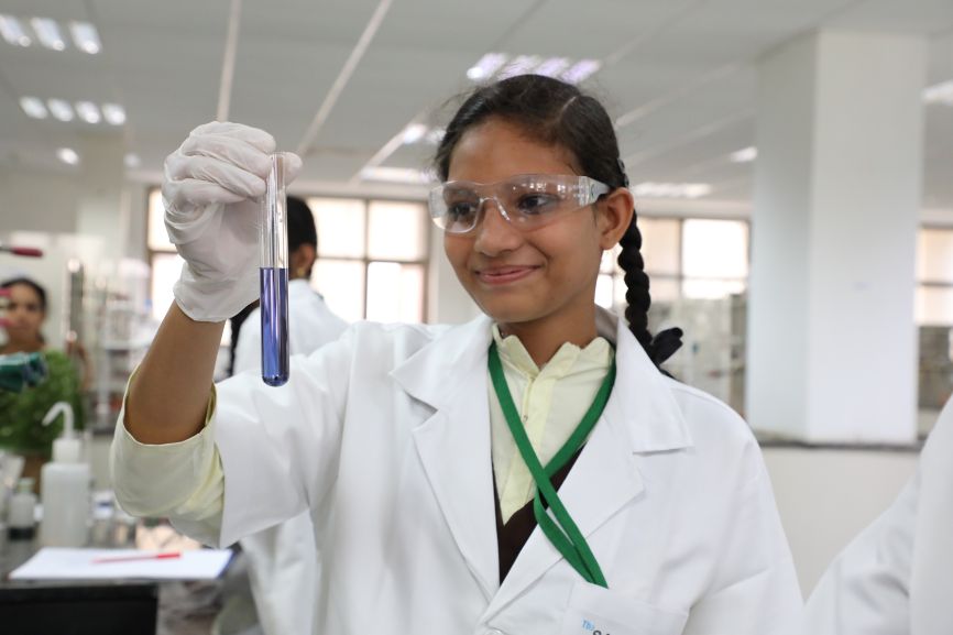 A smiling young girl holds up a test tube