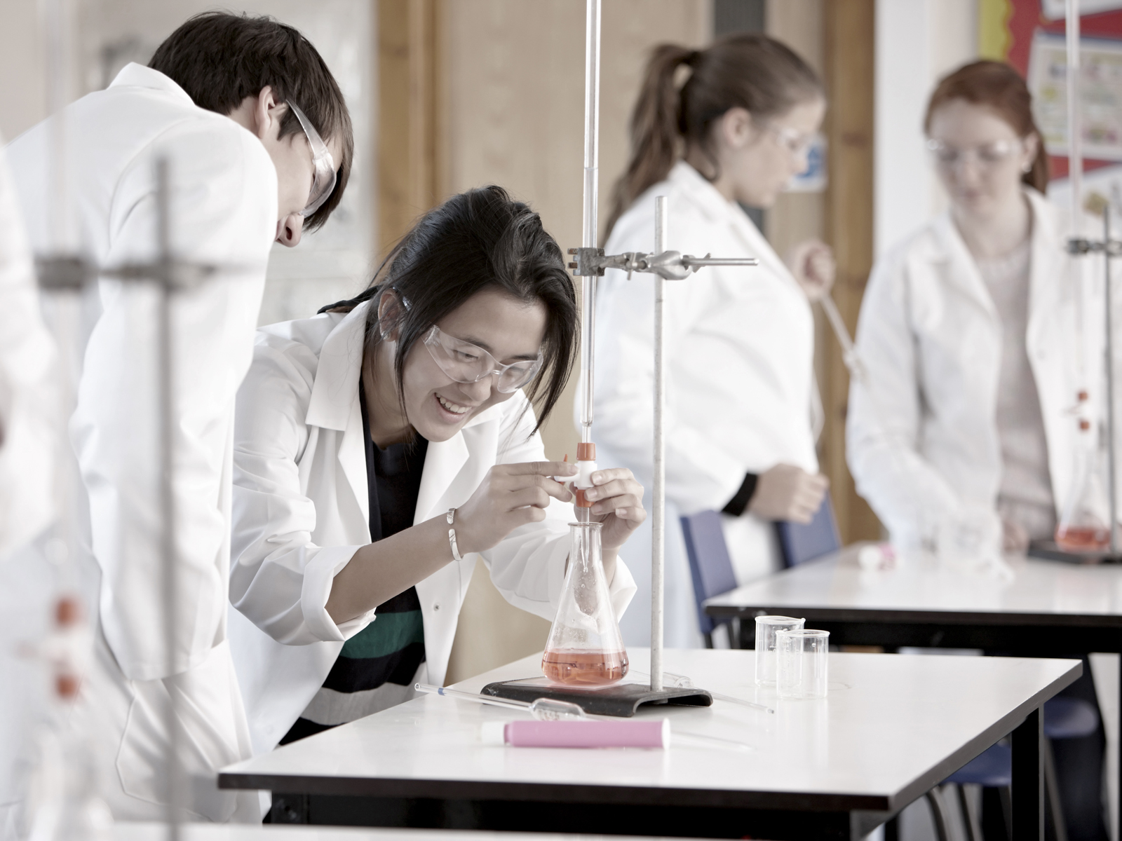 Three students under the supervision of a teacher watch clouds of steam coming out of a beaker
