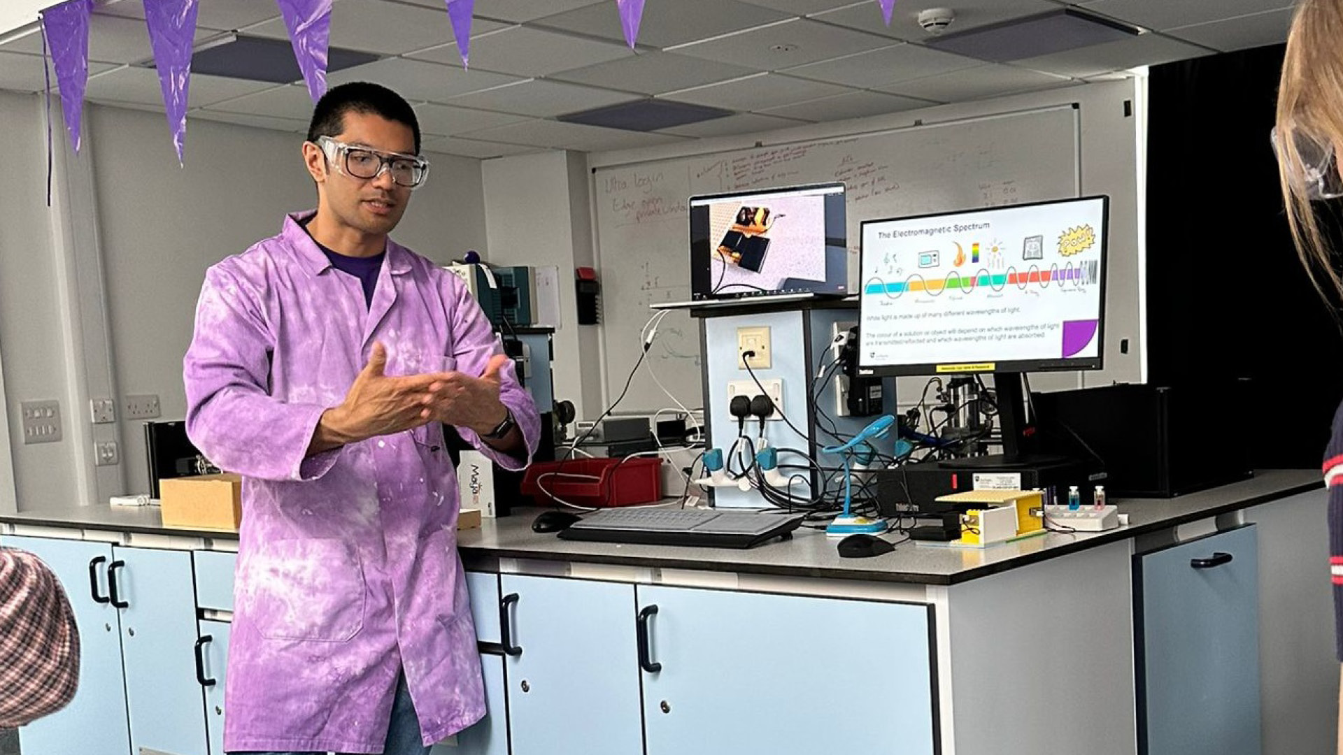 Benjamin Arenas wearing lab coat and glasses explaining to audience out of view