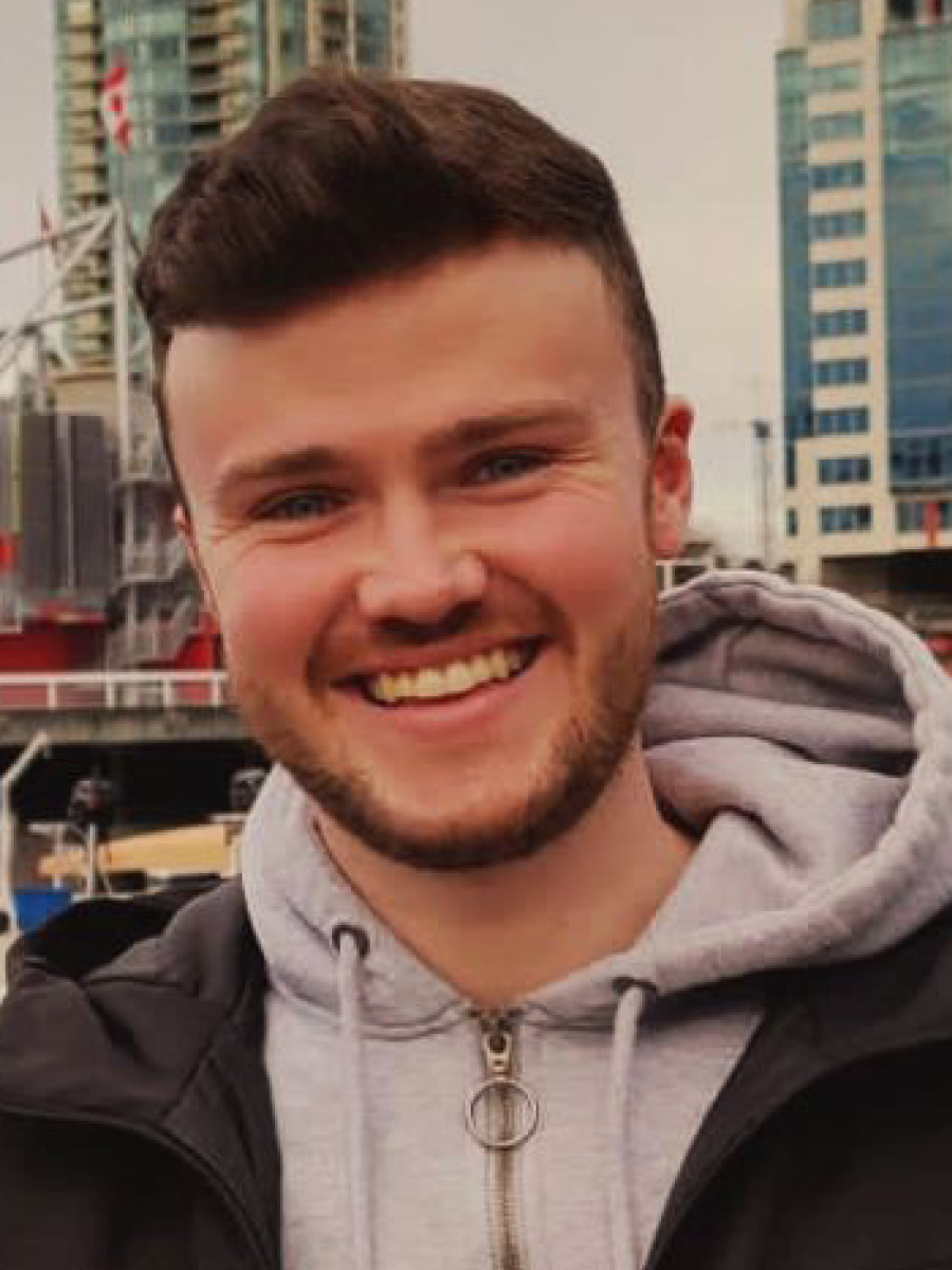 Conor Eivers smiling to camera in a light grey hoody, with short beard