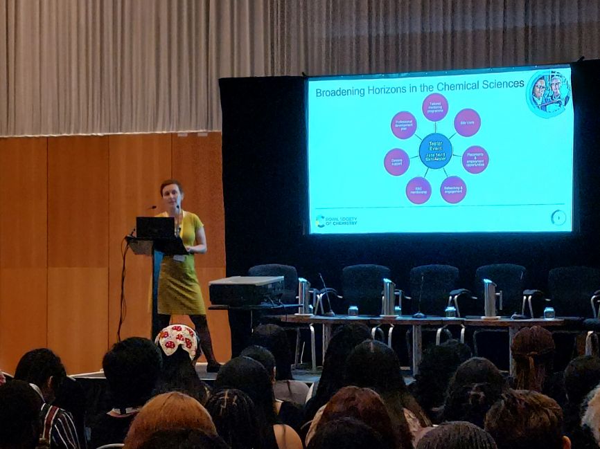 Dr Joanna Jasiewicz gives a speech to the left of a screen showing a graphic with six pink dots and a blue dot