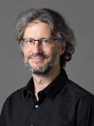Igor Larrosa wearing rectangular glasses and a black shirt, set against a solid dark gray background.