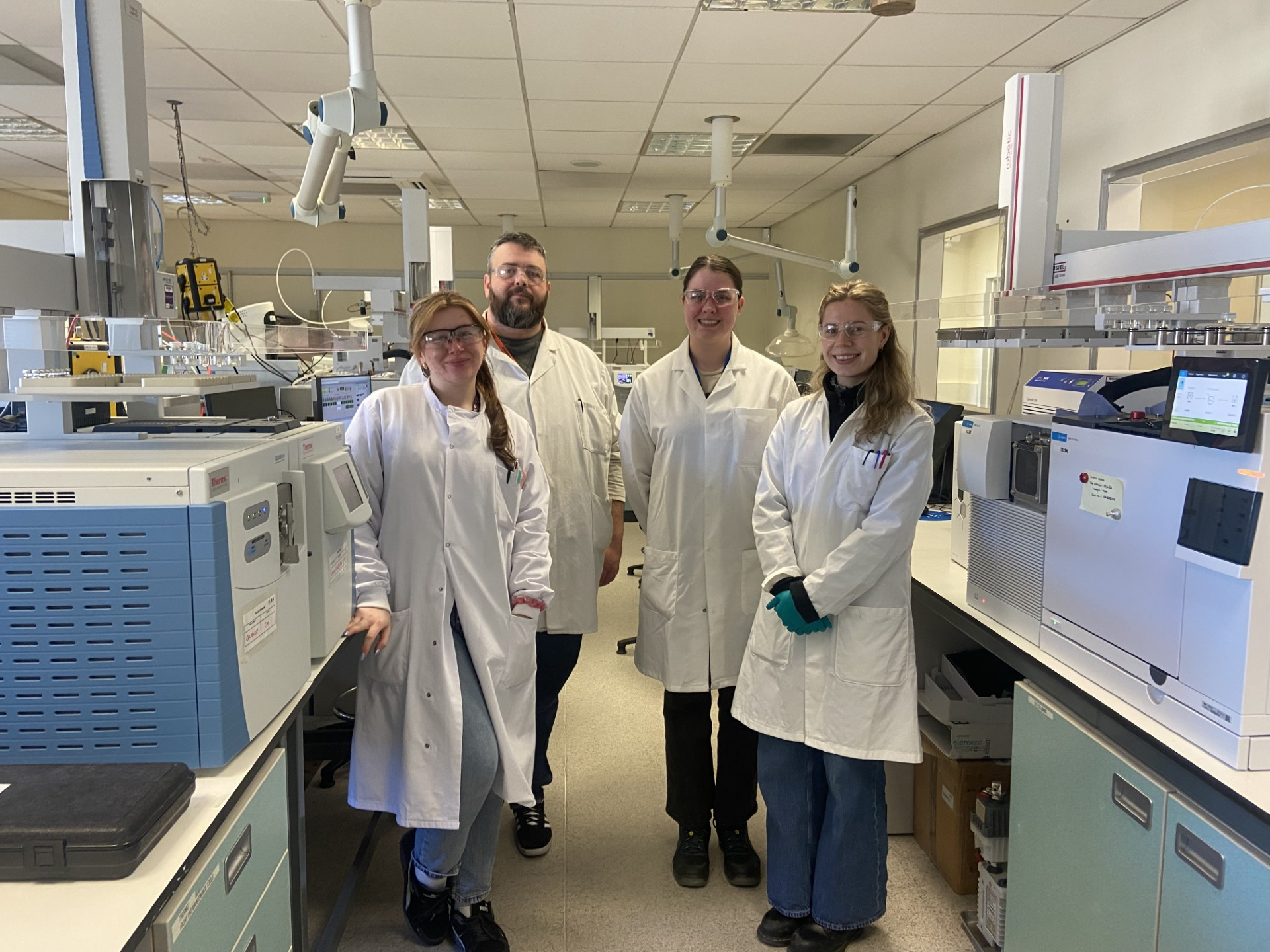Four members of the Scottish Water team stand in white lab coats and goggles in their laboratory