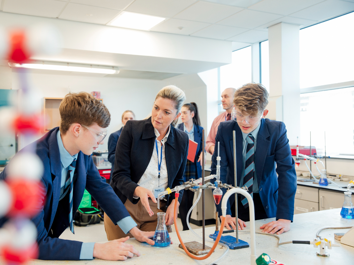 Teacher with pupils in school uniform at a science bench in classroom
