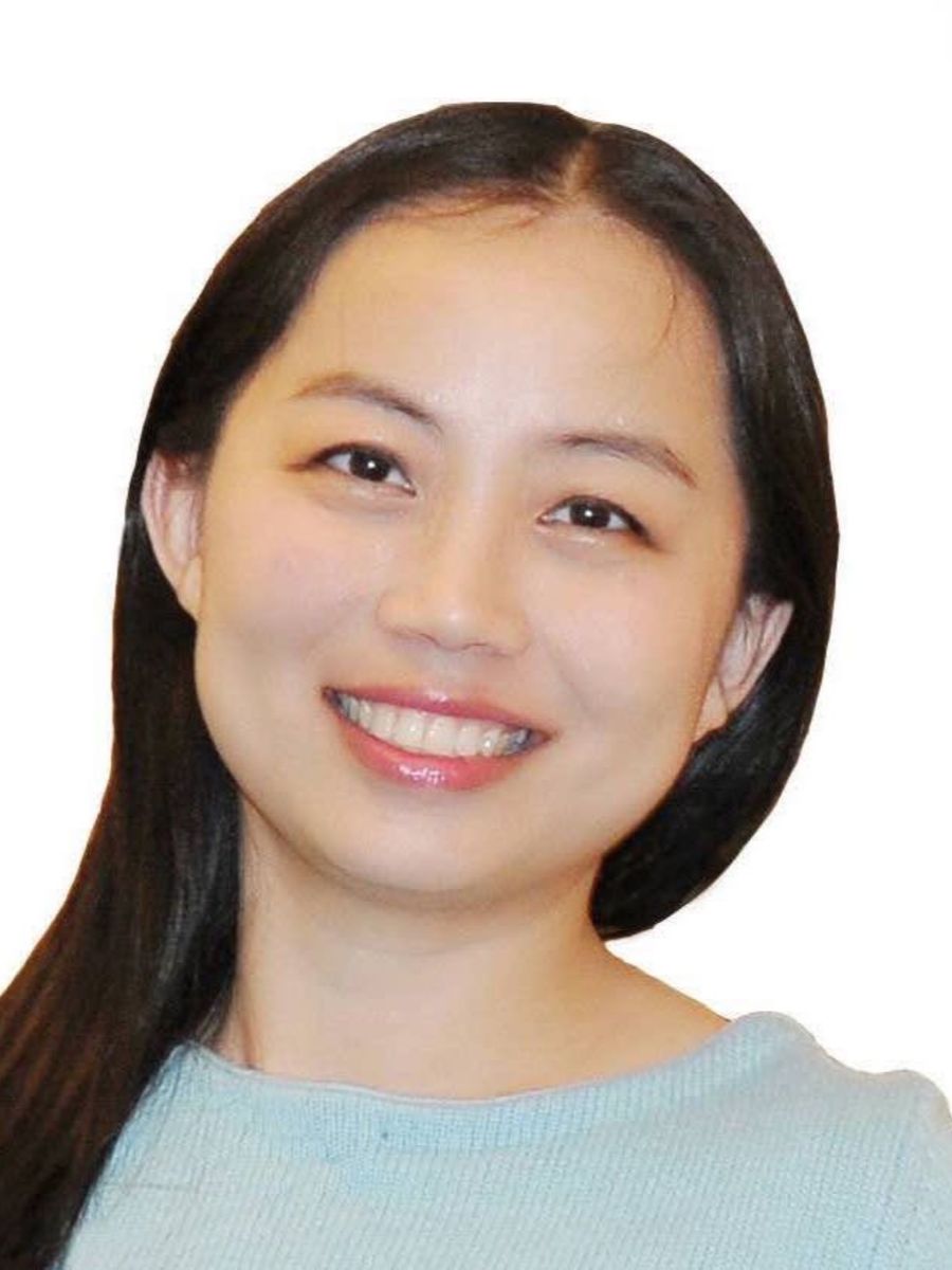 Jun Fan smiling to camera with long dark hair and wearing green sweater