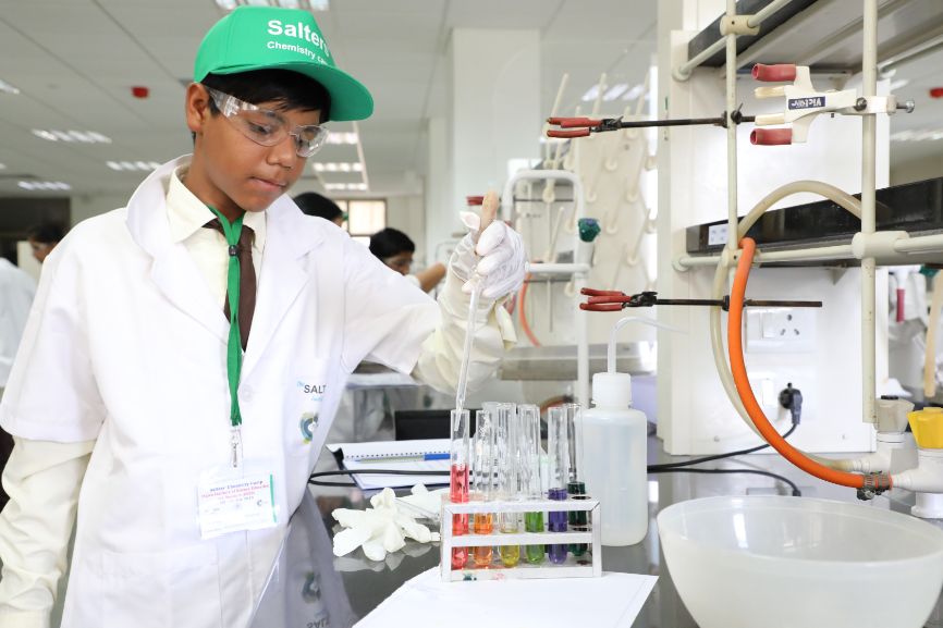 A boy holds a pipette over a series of test tubes filled with multi-coloured liquid
