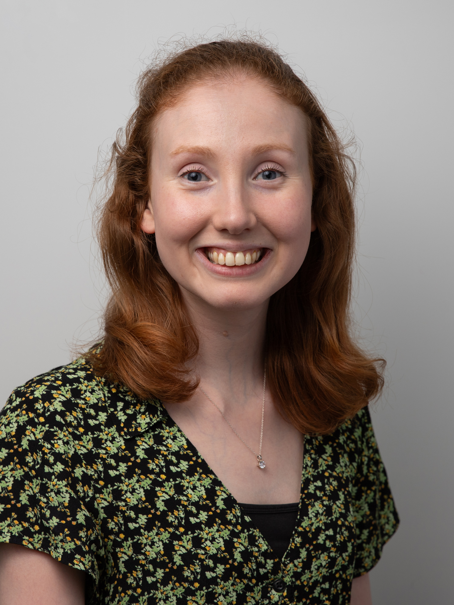 Emma Carlisle wearing a dark green and yellow V-neck blouse set against a plain gray background.
