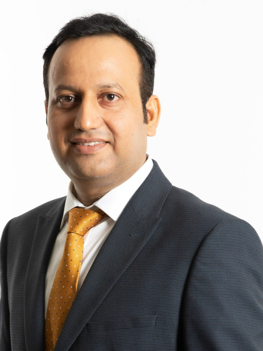 Adarsh Kumar Pandey smiling to camera wearing suit and gold tie