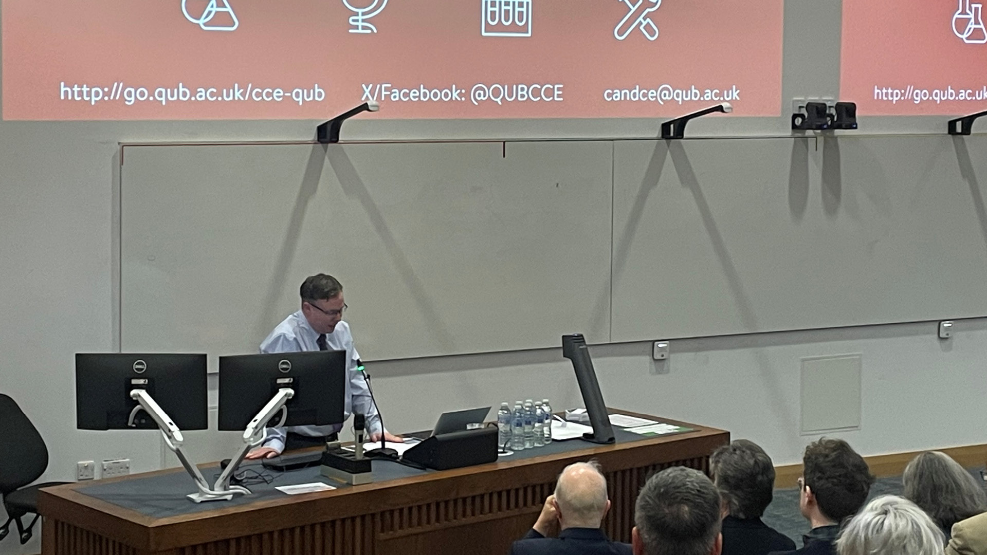 Kevin Morgan presenting behind large desk to large audience