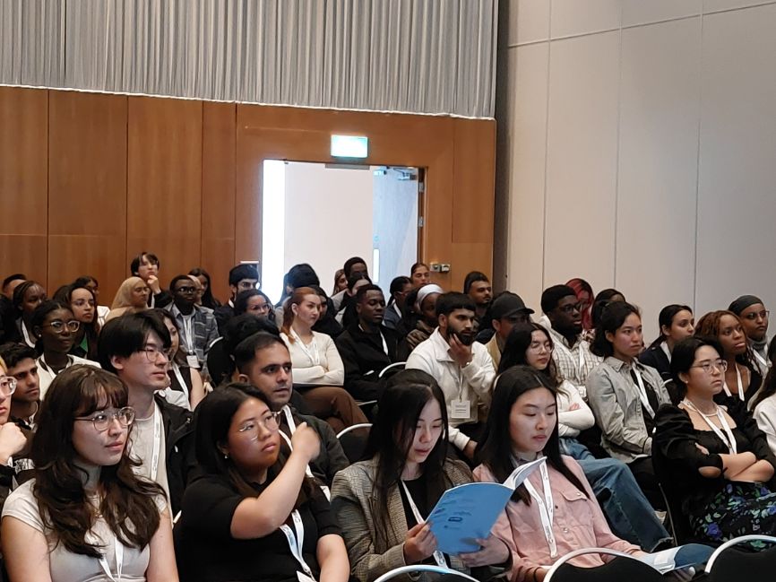 Dozens of students and young chemical scientists sit in a large hall facing a stage, which is out of shot