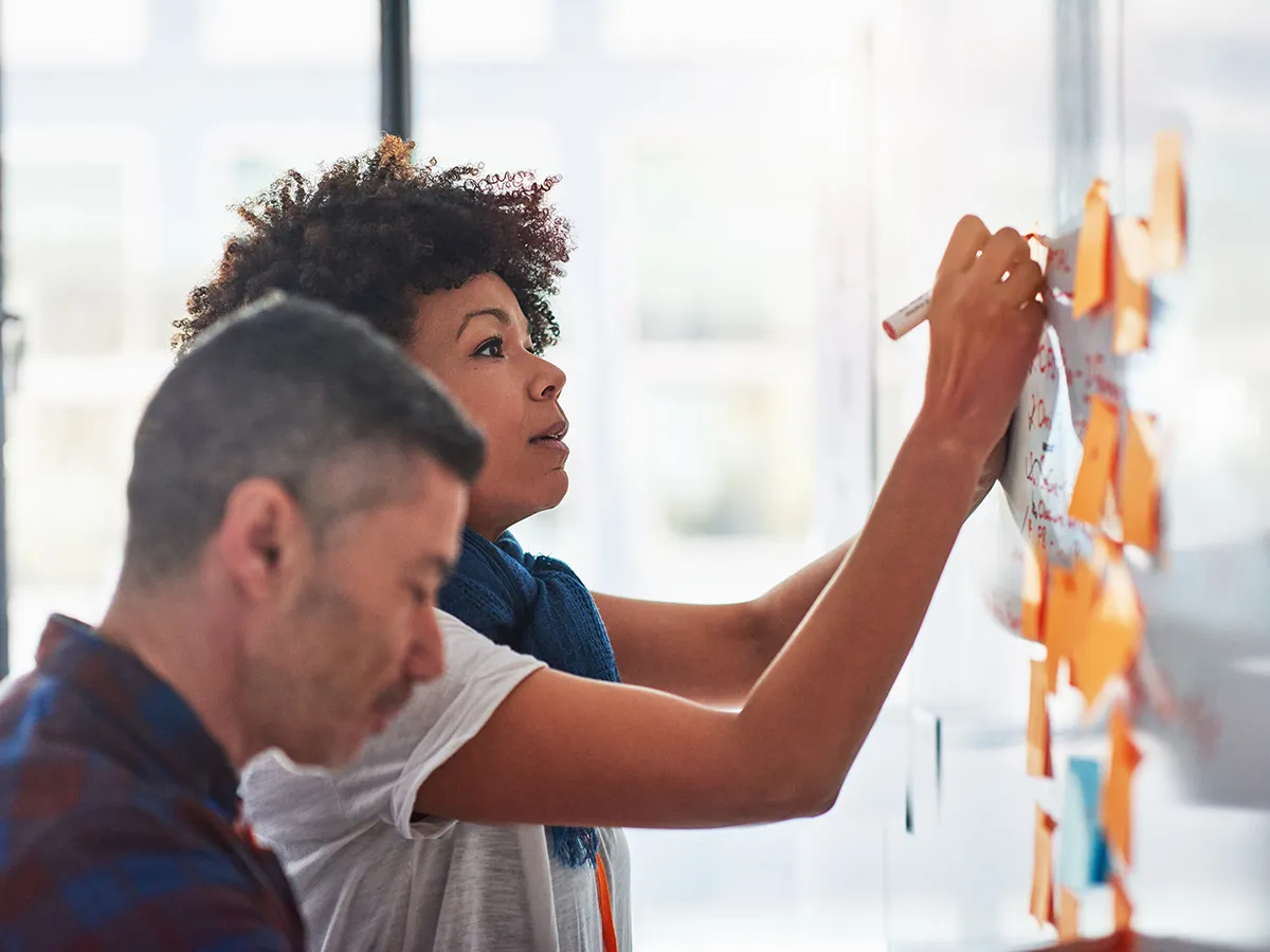 Two people interacting with post-in notes on a whiteboard Two people interacting with post-in notes on a whiteboard