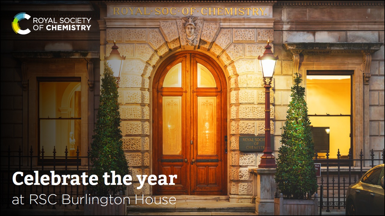 The entrance of the Royal Society of Chemistry at Burlington House at night, featuring two lit lamp posts and decorated Christmas trees.
