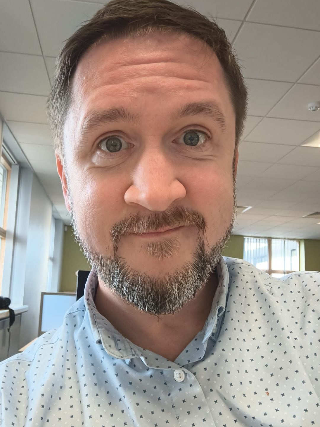 Michael Rowan smiling to camera with beard and wearing spotted shirt