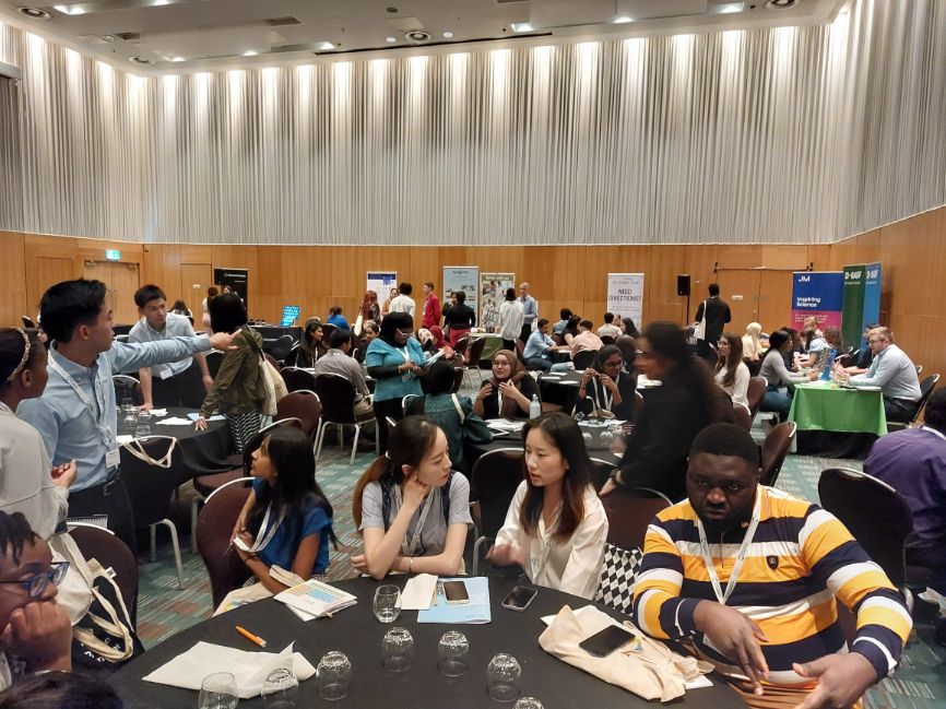 Students mingle at tables at stalls in a large conference room