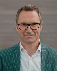 Darren Dixon, recipient of the Royal Society of Chemistry's Charles Rees Award, with glasses and a green pinstripe jacket smiling at the camera.