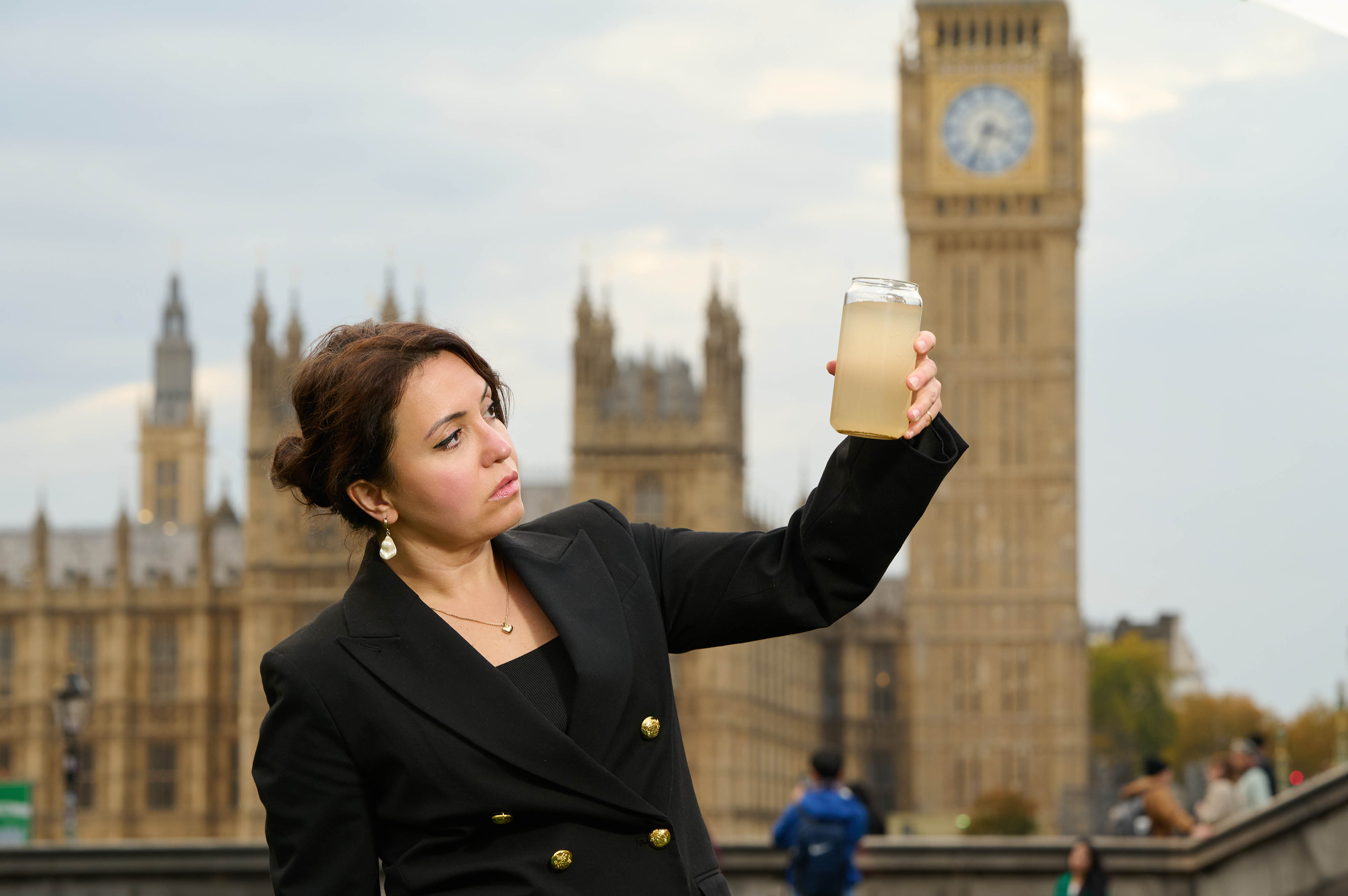 Burcu Yesilyurt holds a cup of off-yellow water from the River Thames in front of the Palace of Westminster