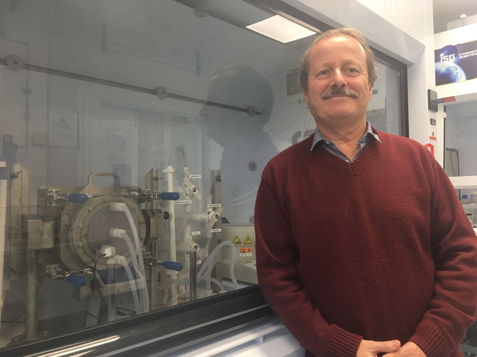 Professor Canham stands in front of a fume hood smiling at the camera