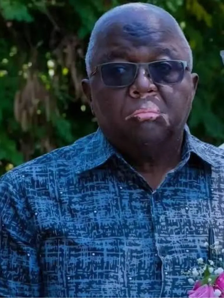 Jacob Midiwo portrait - deceased Jacob Midiwo wearing glasses and a blue patterned shirt