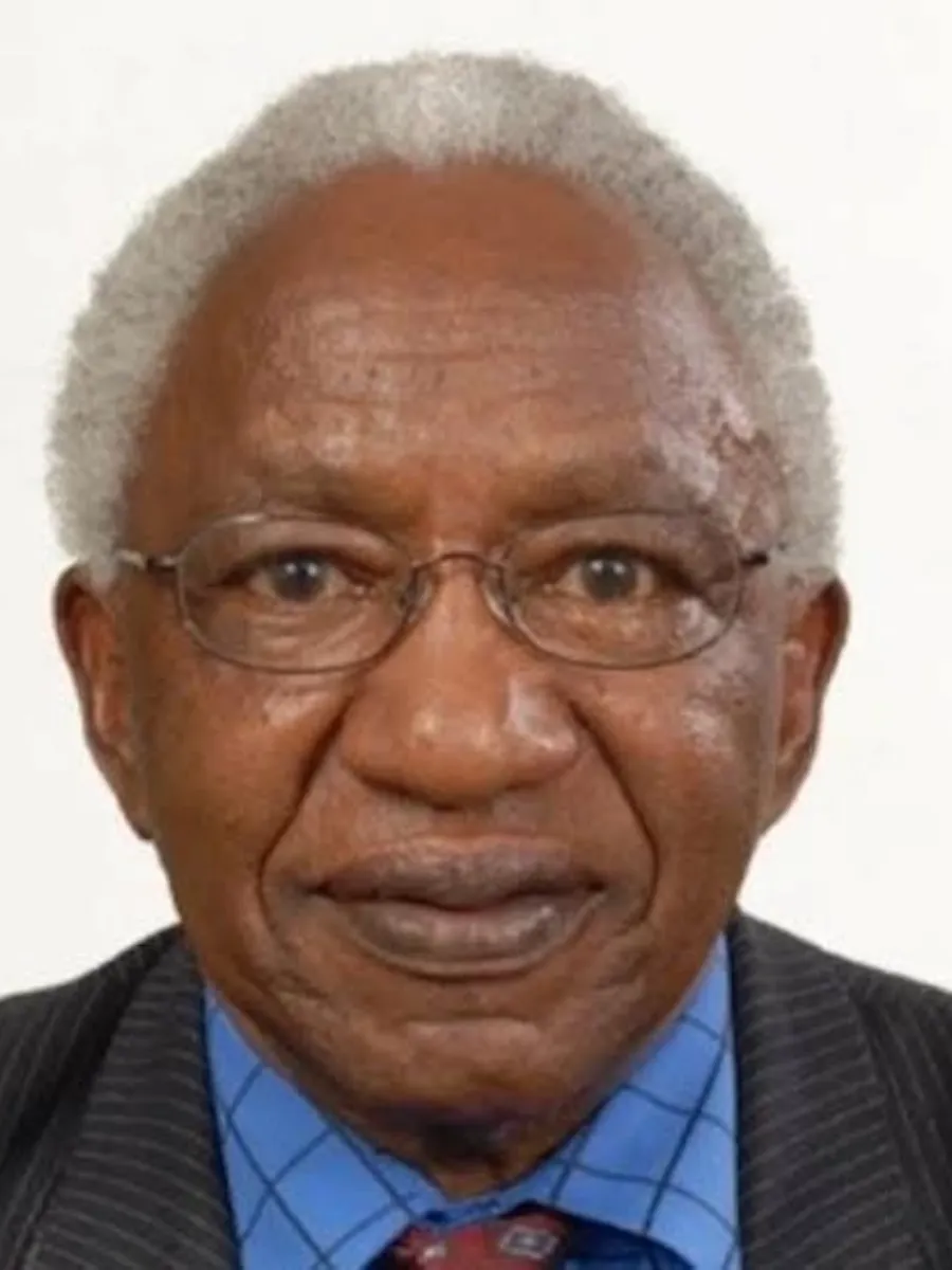 Shem Wandiga portrait - deceased Shem Wandiga smiling to camera wearing glasses, blue shirt and tie and suit jacket
