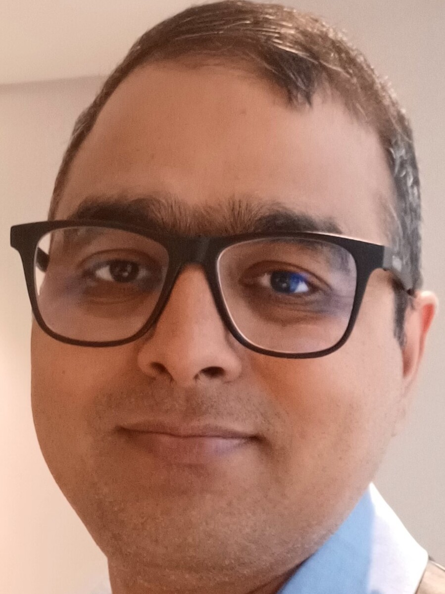 Vinod Kumar smiling to camera in close up, wearing glasses