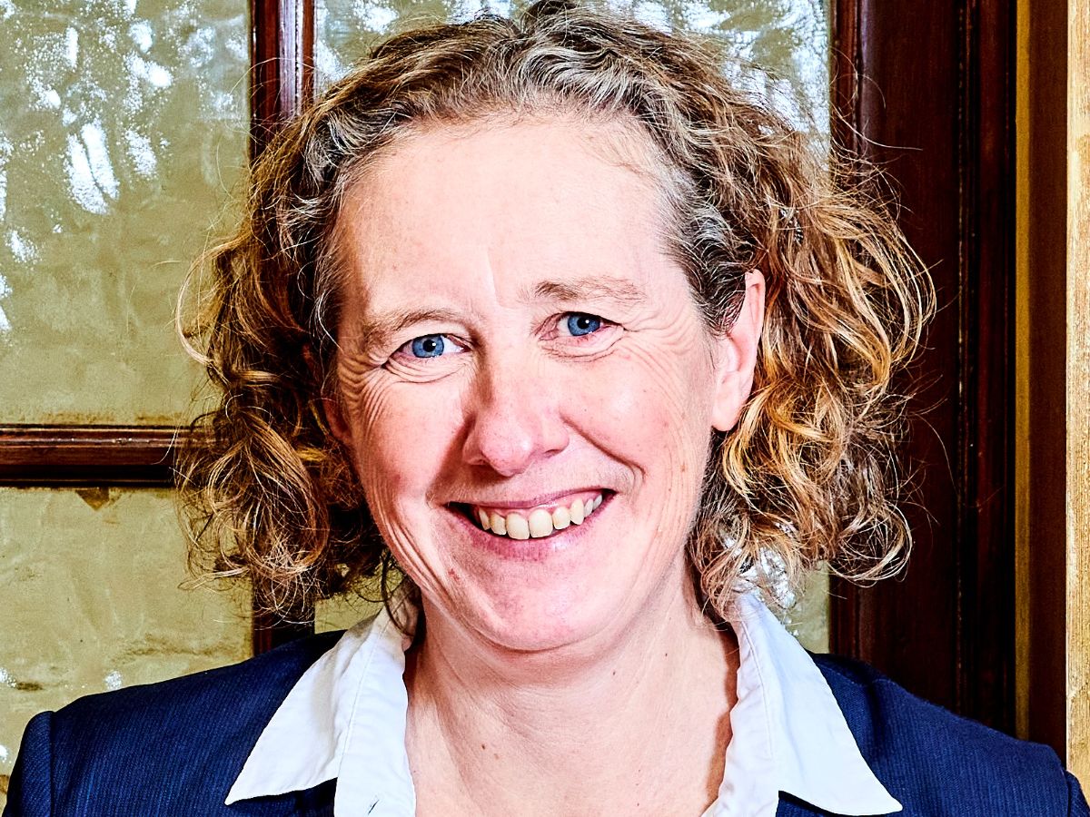 A picture of Professor Candy Rowe smiling in front of a wooden door with glass panels