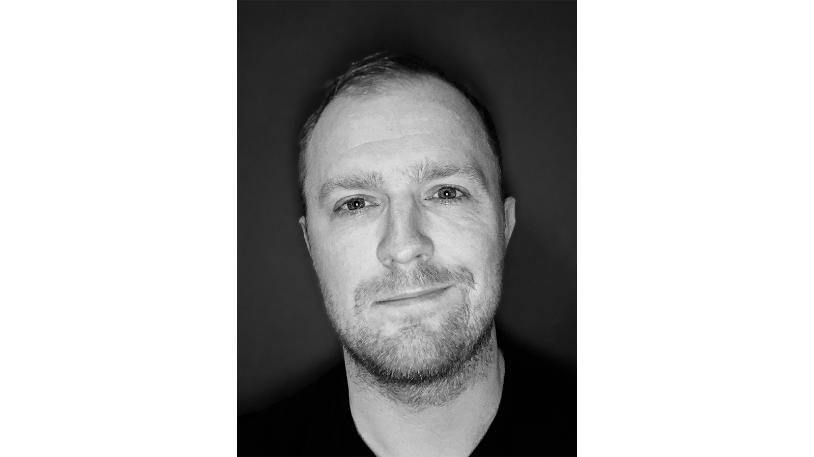 Black and white image of Dr Jon Major with a beard and mustache smiling for camera