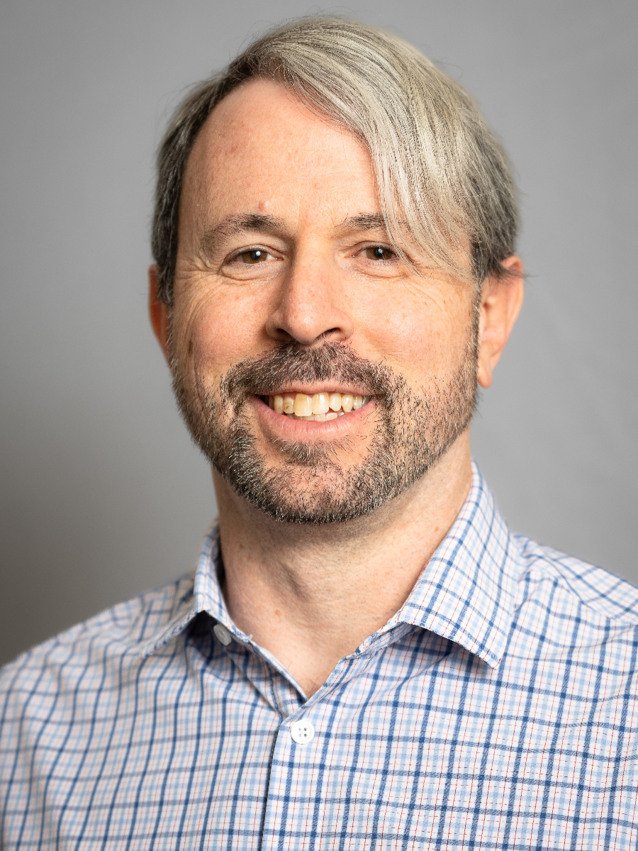 Matt Sigman smiling to camera with beard,  in checkered white and blue shirt