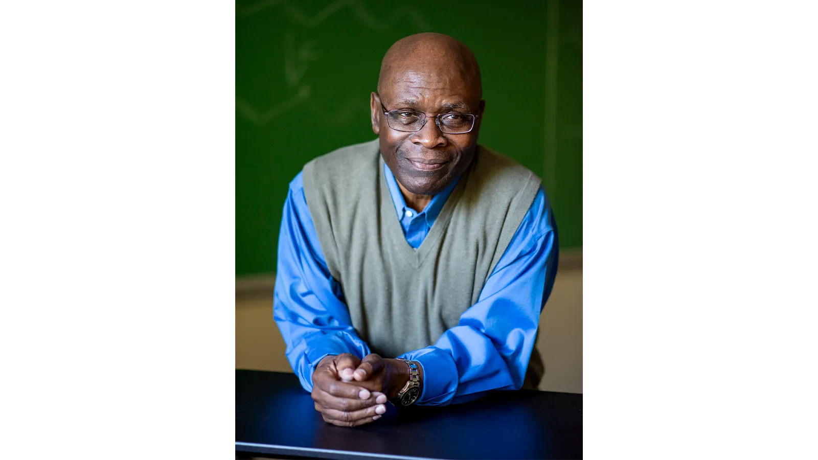 Professor Samson Jenekhe sitting at a desk in blue shirt and glasses, smiling for camera