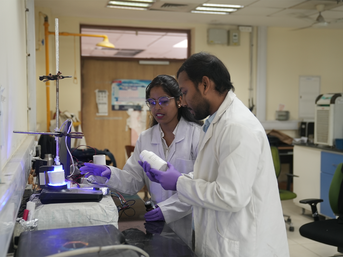 Two of AEEon Collective team in lab coats and gloves, looking at a scientific equipment
