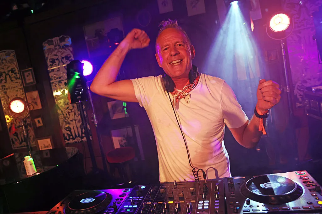 GettyImages-2281431639 - Fatboy Slim 2 Fatboy Slim - aka Norman Cook - poses with headphones and a microphone holding his arms up