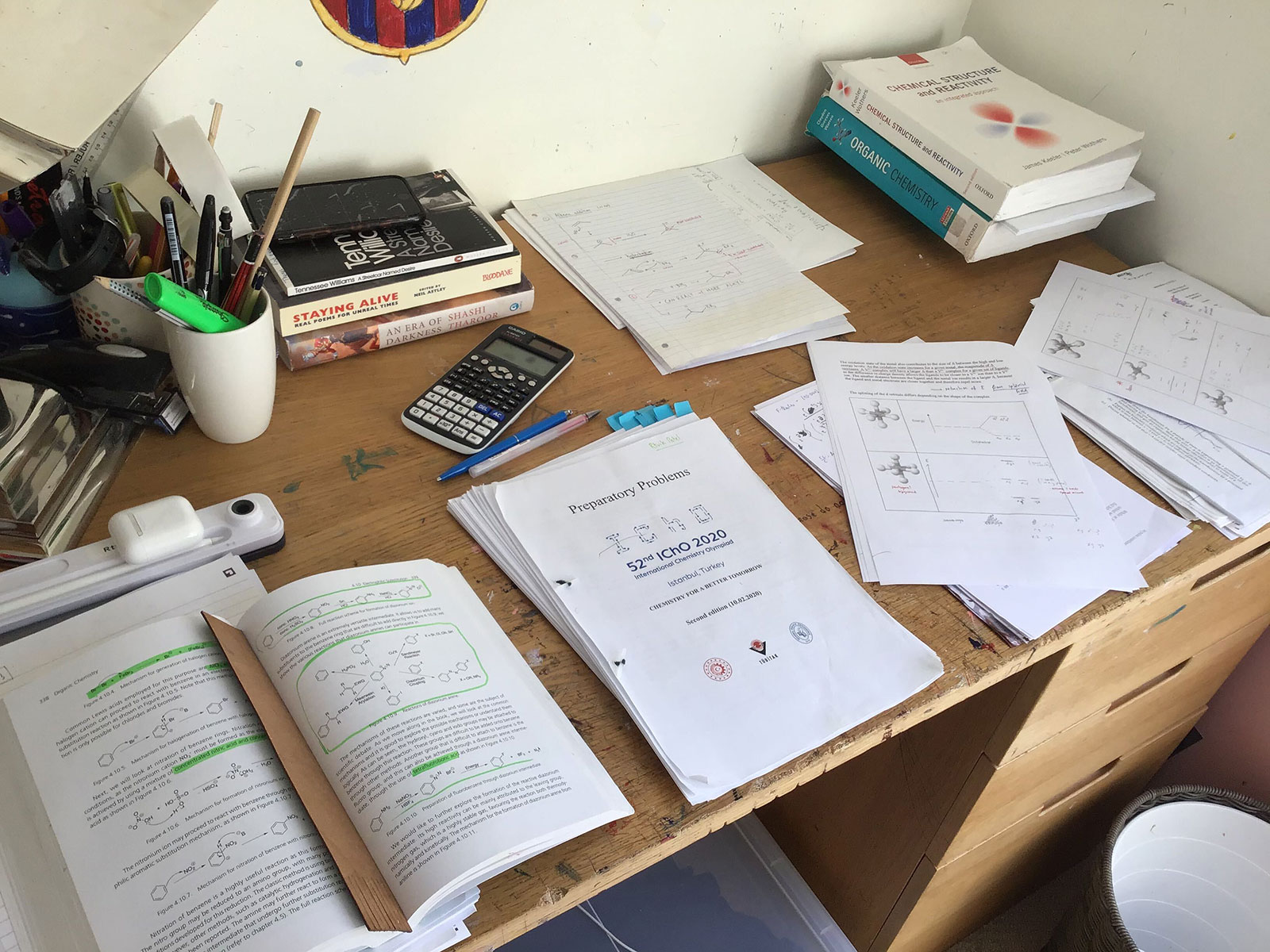 A desk with writing materials and sheets of paper containing chemistry questions.