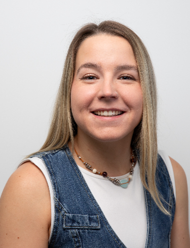 Sophie Orchard, smiling, wearing a denim vest over a white top against a plain grey background.