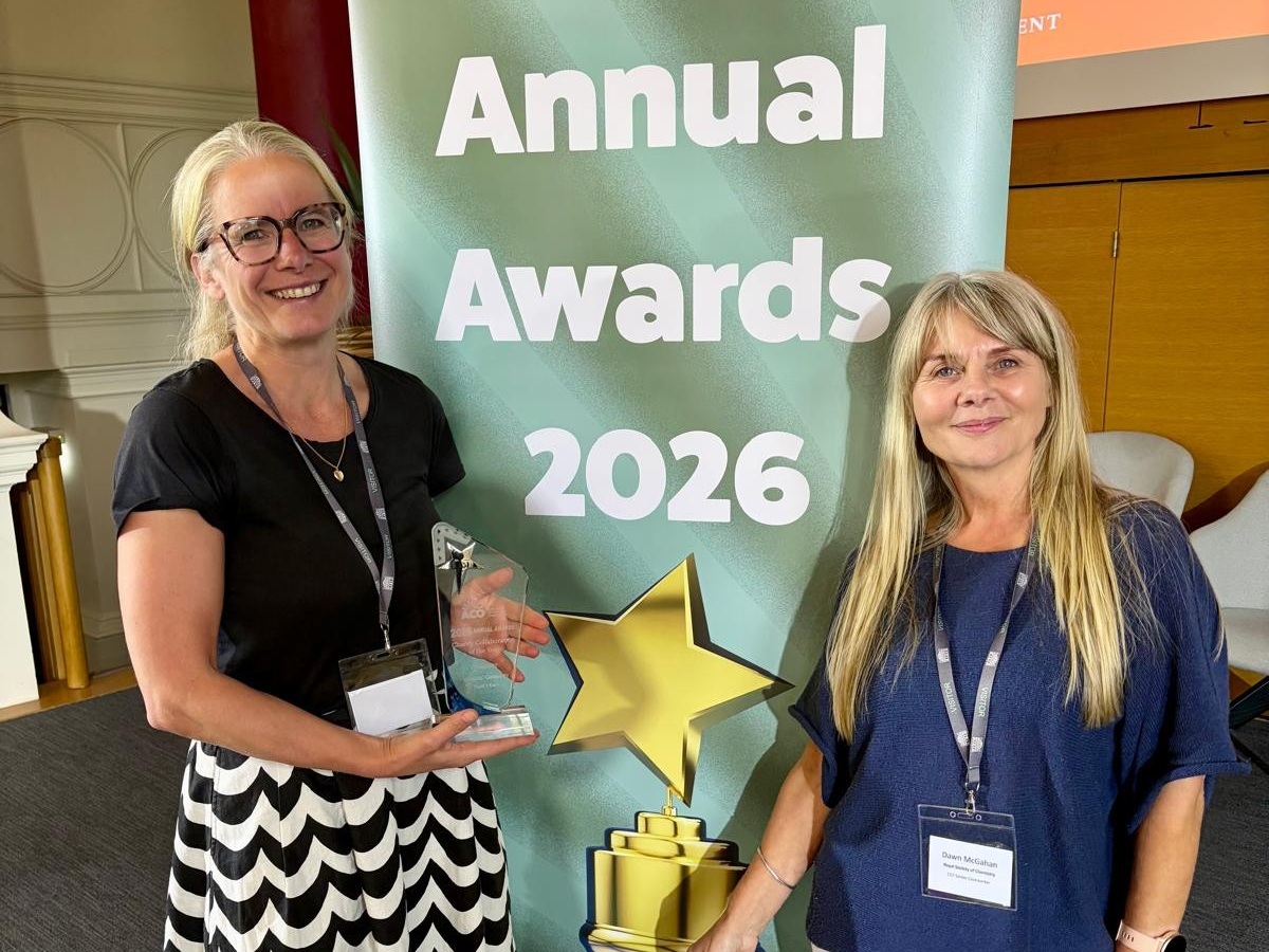 Maggie Houghton and Dawn McGahan standing next to a sign reading "ACO Annual Awards 2026" with Maggie holding a glass trophy