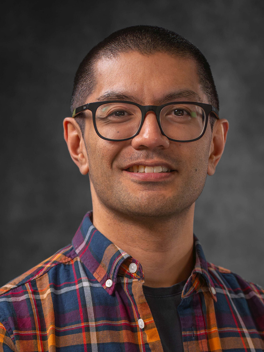 Benjamin Arenas smiling to camera in check shirt and glasses