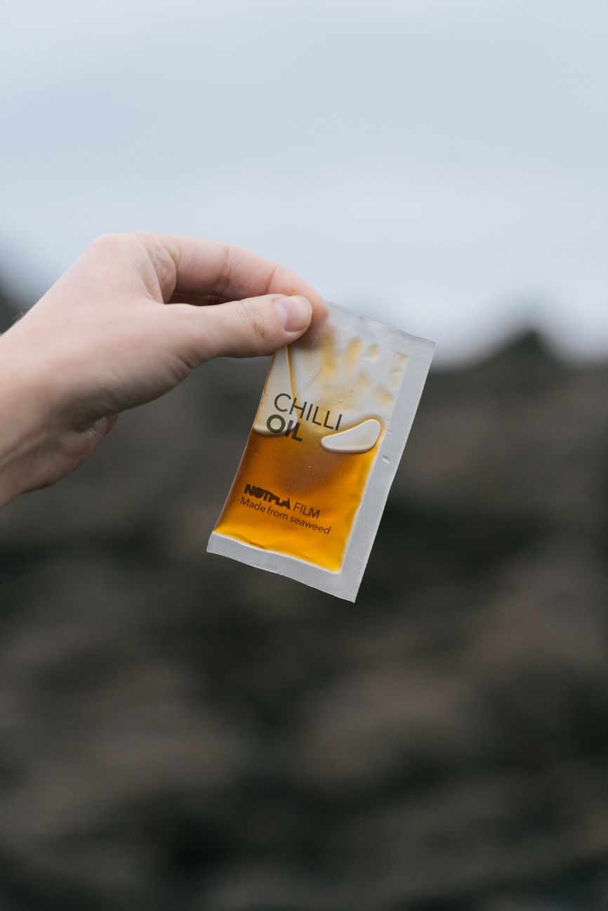 A hand holds a packet of Notpla Film, which contains chilli oil