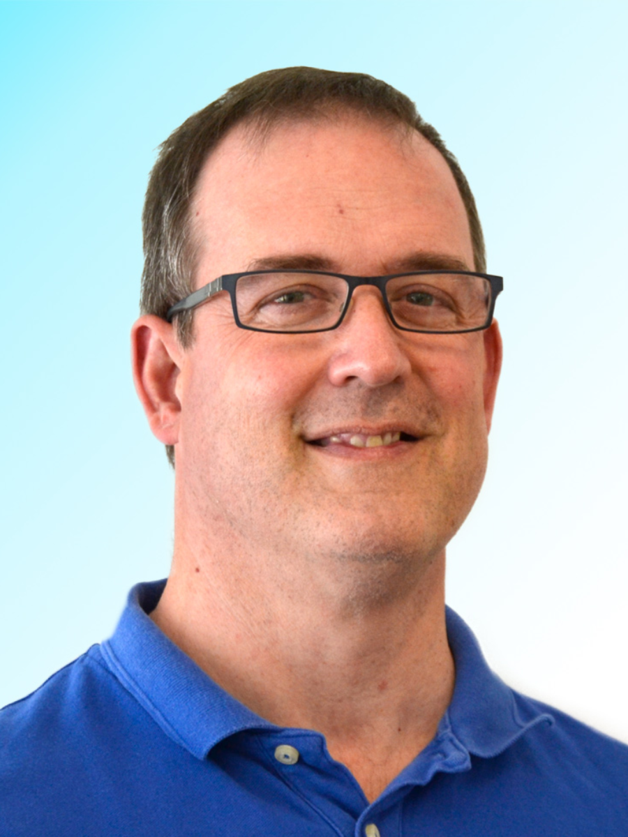 Simon Lancaser smiling at camera wearing glasses and blue polo shirt